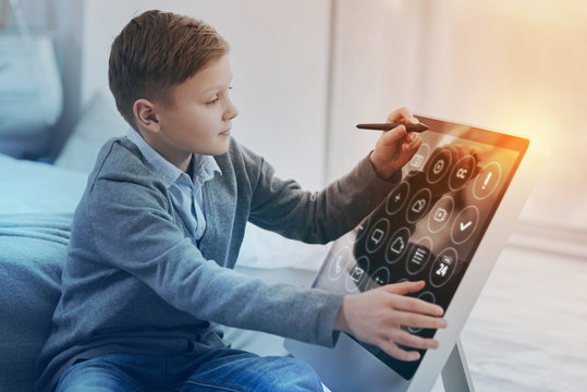Modern childhood. Clever skilled boy holding a modern stylus and using it while doing homework in his computer