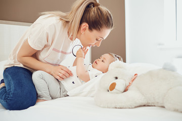 Mother with baby lying on the bed in a white room.