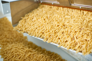 Close up shot of dry macaroni spilling from machine unit on modern food production factory, copy space