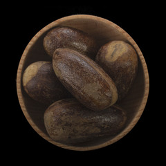 nutmegs in wooden cup isolated on black background. top view