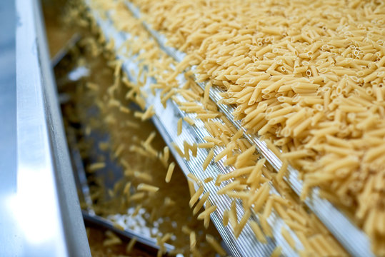 Close Up Of Dry Macaroni Spilling From Machine Unit On Modern Food Production Factory, Copy Space