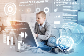 Amazing opportunities. Emotional clever boy sitting in front of a large screen and feeling impressed by his new powerful computer