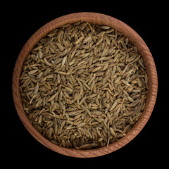 cumin in wooden cup isolated on black. top view