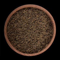 cumin in wooden cup isolated on black. top view