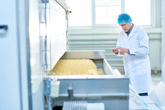 Portrait of senior factory worker doing  quality inspection in food plant standing by machine unit with macaroni, copy space