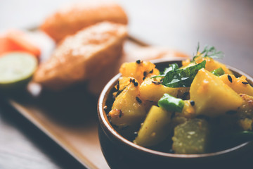 Chatpate Masala Aloo Sabzi fry OR Bombay potatoes served with fried puri or Indian bread made up of wheat in a plate, selective focus