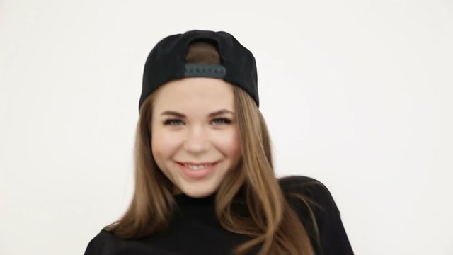 a teenage girl in black hip-hop clothes and a cap dances at the white wall- close-up, handheld shoot, small depth of field