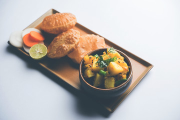 Chatpate Masala Aloo Sabzi fry OR Bombay potatoes served with fried puri or Indian bread made up of wheat in a plate, selective focus