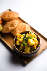 Chatpate Masala Aloo Sabzi fry OR Bombay potatoes served with fried puri or Indian bread made up of wheat in a plate, selective focus