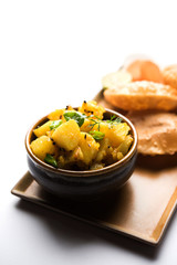 Chatpate Masala Aloo Sabzi fry OR Bombay potatoes served with fried puri or Indian bread made up of wheat in a plate, selective focus