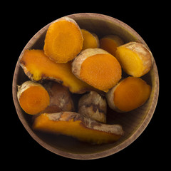 fresh turmeric in wooden cup isolated on black. top view
