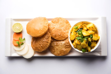 Chatpate Masala Aloo Sabzi fry OR Bombay potatoes served with fried puri or Indian bread made up of wheat in a plate, selective focus