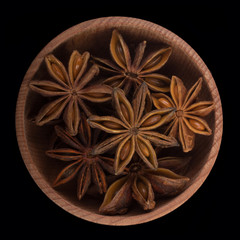 star anise (badian) in wooden cup isolated on black. top view
