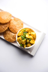 Chatpate Masala Aloo Sabzi fry OR Bombay potatoes served with fried puri or Indian bread made up of wheat in a plate, selective focus