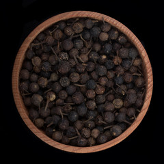 cubeba peppercorn in wooden cup isolated on black. top view