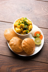 Chatpate Masala Aloo Sabzi fry OR Bombay potatoes served with fried puri or Indian bread made up of wheat in a plate, selective focus