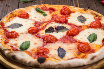 rustic italian pizza Margarita with mozzarella, cherry tomatoes and basil leaves on wooden background