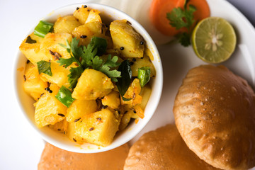 Chatpate Masala Aloo Sabzi fry OR Bombay potatoes served with fried puri or Indian bread made up of wheat in a plate, selective focus
