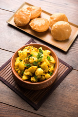 Chatpate Masala Aloo Sabzi fry OR Bombay potatoes served with fried puri or Indian bread made up of wheat in a plate, selective focus
