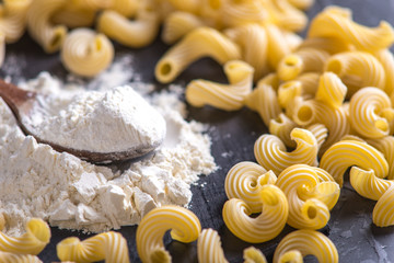 Uncooked pasta cavatappi with flour from durum wheat on a dark background. Concept of The composition of food design.