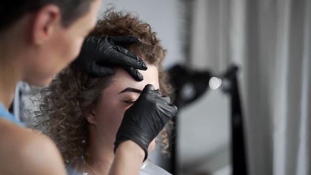 Stylist wipes eyebrows with a sponge after eyebrow coloring at the beauty salon, eyebrow coloring and correction, coloring by henna, beauty and healthcare, cosmetic services