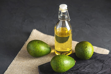 Avocado fruit and oil in glass bottle on dark background. Concept organic eco products for food and...