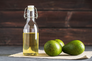 Avocado fruit and oil in glass bottle on dark background. Concept organic eco products for food and...