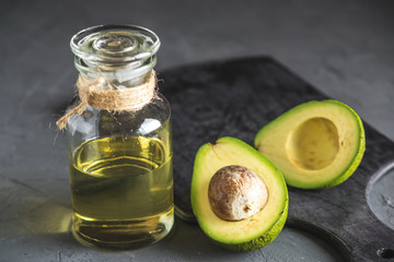 Avocado fruit and oil in glass bottle on dark background. Concept organic eco products for food and...