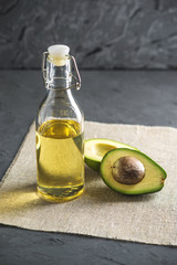 Avocado fruit and oil in glass bottle on dark background. Concept organic eco products for food and cosmetic procedures