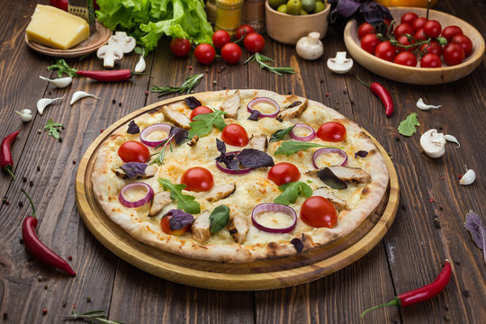 Italian Pizza with chicken, cherry tomatoes, cheese and onions on the board decorated with leaves of arugula and basil