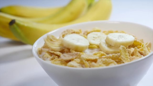 Corn flakes with milk are in a bowl. pieces of banana fall on the top of this delicious breakfast. Close-up shot