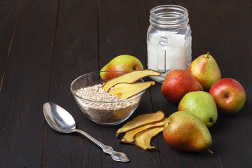 bowls with healthy breakfast and pears on a wooden table. Homemade granola with yoghurt and fruits standing on a black table. Oat meals in a bowl with green pears