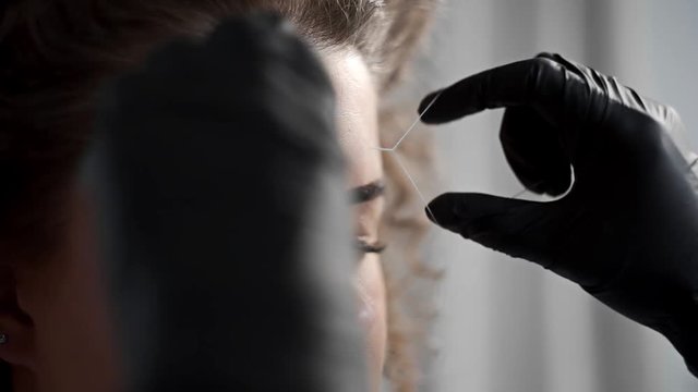 Removing small hairs from face with thread in beauty salon, depilation with thread, threading in beauty salon, facial treatment, cosmetic manipulations