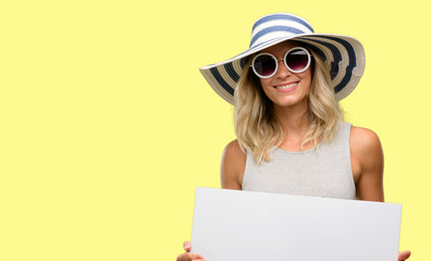Young woman wearing sunglasses and summer hat holding blank advertising banner, good poster for ad,...