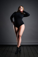 Plus size sexy model in black bodysuit, fat woman on gray studio background, overweight female body