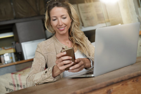 Businesswoman using smartphone in front of laptop, sitting at coffeeshop