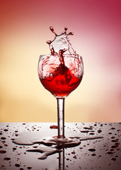 Splash of drink in the wineglass, splashes and spilled water, gradient background, drops on the glass