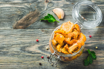 Marinated chanterelle mushrooms in glass jar on rustic background. Top view, space for text.