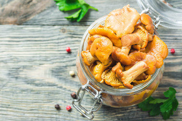 Marinated chanterelle mushrooms in glass jar on rustic background. Top view, space for text.