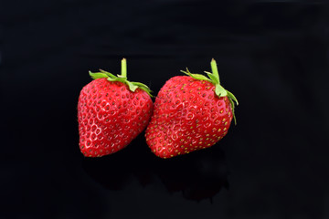 Closeup of two fresh red strawberries on a black background.  selective soft focus