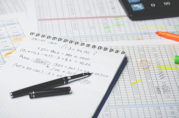 Paper notebook with accounting calculations and pen on the background of a table with numbers