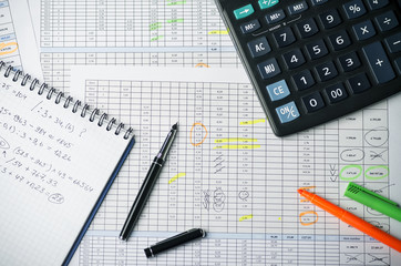 Tables with accounting calculations, paper notebook with records, calculator, pen and highlighter
