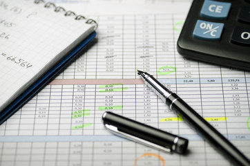 Accounting records in tables, a paper notebook with calculations and a black pen
