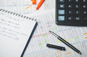 Accounting records in tables, a paper notebook with profit calculations, a pen and a calculator