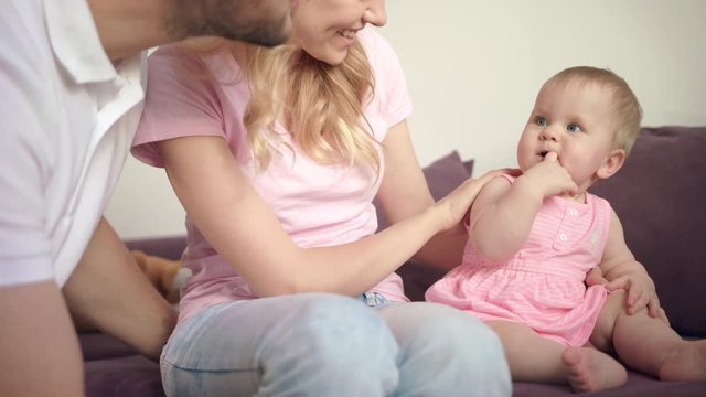 Happy family with baby playing together. Cute baby with finger in mouth smiling with mom and dad. Infant playing with parents. Sweet parenting. Cute toddler have fun at home. Family love concept