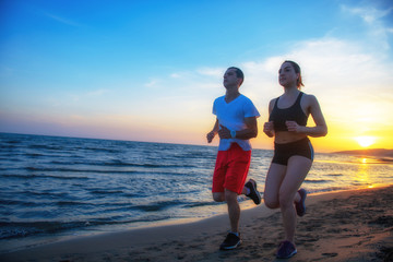 Man and women running on tropical beach at sunset