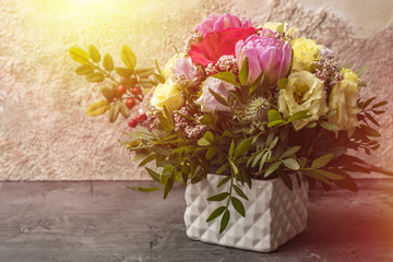 A beautiful bouquet of roses and other flowers in a white vase, on a light background