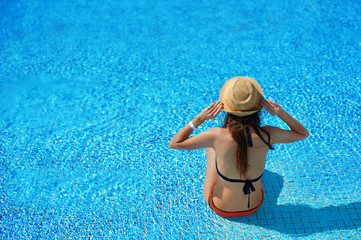 Woman in a straw hat relaxing on a deck-chair near a luxurious summer pool in hotel, concept time to travel