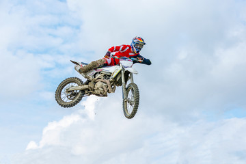 racer on a motorcycle in flight, jumps and takes off on a springboard against the sky.