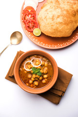 Chole Bhature or Chick pea curry and Fried  Puri served in terracotta crockery over white background. selective focus